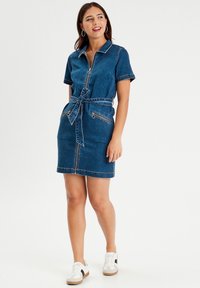 Abito in denim con zip frontale, maniche corte, vita definita e tasche laterali con zip. Tessuto blu scuro con dettagli di cucitura in contrasto.