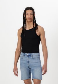 Un top fără mâneci negru cu textură ribbed și pantaloni scurți din denim albastru deschis. Pantalonii scurți au tivuri răsucite și un design cu cinci buzunare, cu o ușoară decolorare.