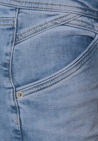 Kapsa na džíny, světle modré barvy, s kontrastním prošíváním, detail kovového knoflíku a mírně strukturovaný povrch látky.