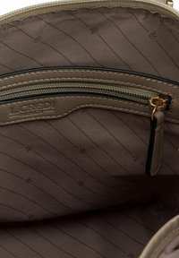 Interno di borsa beige con una tasca con zip. La fodera in tessuto testurizzato presenta sottili righe diagonali. Logo impresso sul tessuto.