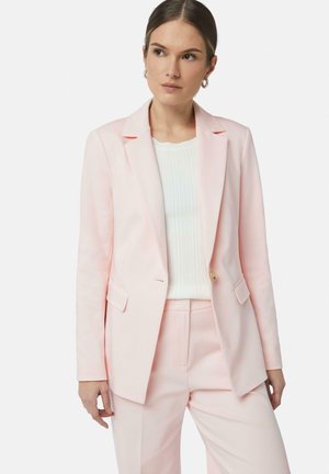 Lichtroze getailleerde blazer met geschikte revers, een enkele knop en twee voorzakken. Gecombineerd met een witte ribbel-top en bijpassende broek.
