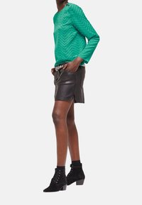 Green textured long-sleeve top, black leather mini skirt, and black suede ankle boots with lace-up design and block heels.