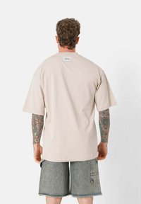 Licht beige oversized t-shirt met korte mouwen, gemaakt van zachte stof. Heeft een label op de achterkant van de halslijn en wordt gecombineerd met grijze denim shorts.
