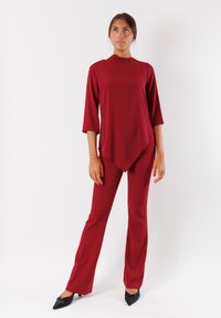 Completo bordeaux composto da due pezzi, con una maglietta a maniche lunghe e orlo asimmetrico e pantaloni aderenti, realizzato in tessuto morbido e leggero.