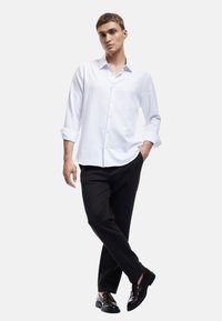 Witte langemouwen shirt met knoopsluiting, gecombineerd met zwarte broeken en glanzende zwarte schoenen. Glad materiaal en getailleerde pasvorm.