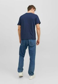 T-shirt de algodón azul marino con cuello redondo y mangas cortas, combinada con jeans de mezclilla azul claro que tienen bolsillos traseros y un corte recto.