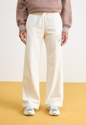 Weißer Fleece-Sweatpants mit Kordelzug und gedrucktem Nike-Logo. Kombiniert mit grau-weißen Sportschuhen. Flacher, weiter Beinansatz.
