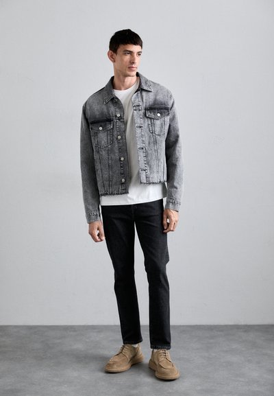 Grå denimjakke med to forsipadser, knaplukning og et falmet look. Parret med en simpel hvid skjorte og mørke jeans.