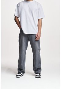 Bílé tričko s krátkými rukávy kombinované se šedými volnými džínami a černo-bílými teniskami. Oblečení má jednoduché, ležérní linie.