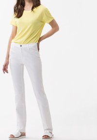 Gul t-shirt med kort ärm som matchas med vita raka byxor. Klädseln har rund hals och en mjuk yta. Vita sandaler fulländar looken.