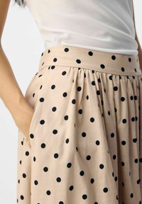 Falda beige con lunares negros, confeccionada en una tela texturada con un diseño fruncido y bolsillos laterales.