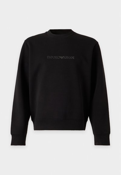 Sweat-shirt noir à manches longues col rond avec un logo Emporio Armani embossé subtil centré sur la poitrine sur un fond uni.