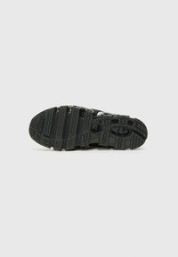 Semelle de chaussure de sport noire en caoutchouc texturé pour l'adhérence, avec des ventilations circulaires et des motifs variés pour la traction et la flexibilité.