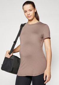 Brun fitted t-skjorte med korte ermer og rund hals, parret med svart treningspose med nettdetaljer. Glatt stofftekstur.
