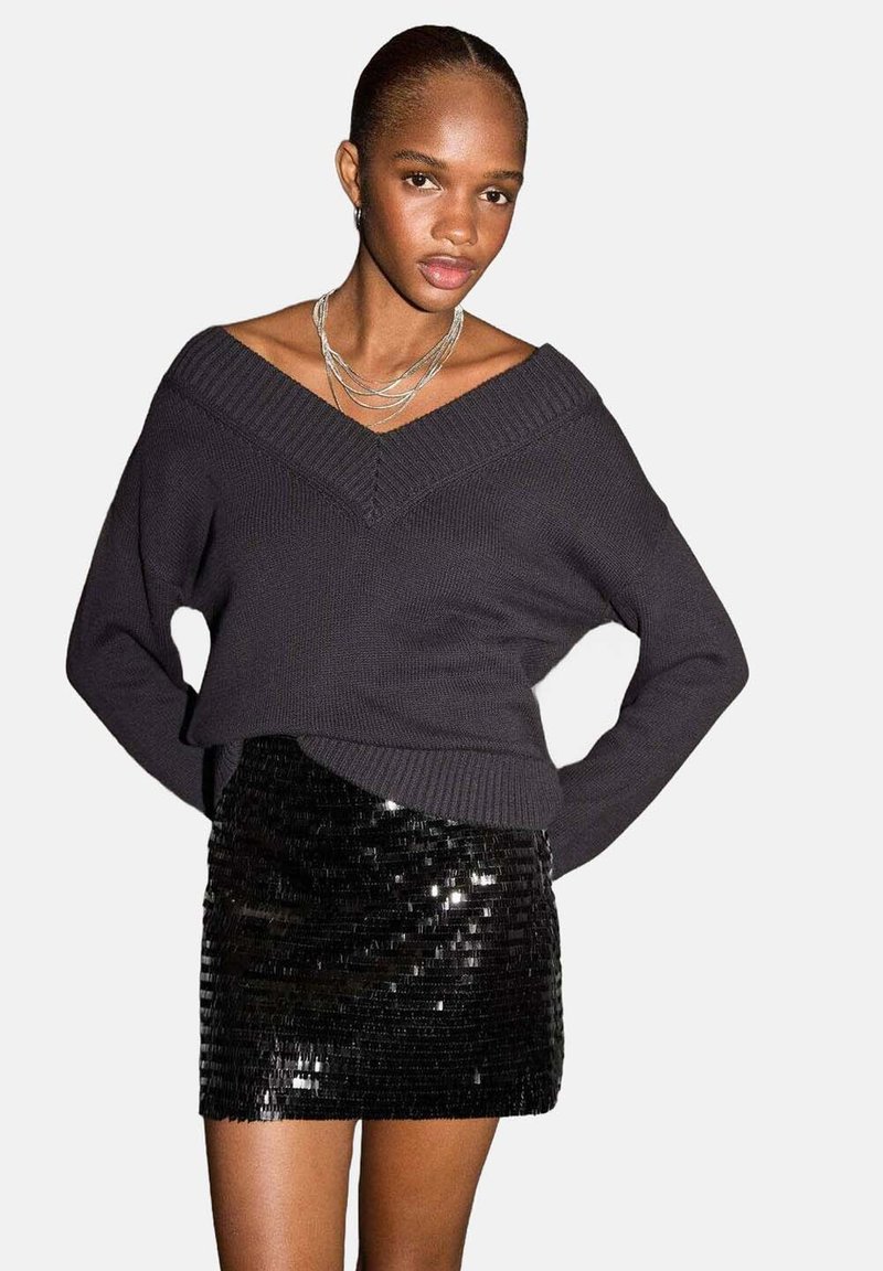 Maglione lavorato a maglia grigio scuro con scollo a V ampio e maniche lunghe, abbinato a una minigonna nera con paillettes, caratterizzata da una silhouette aderente.
