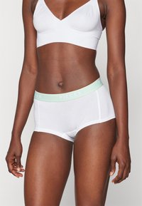 Caleçons en coton blancs avec une ceinture élastique vert menthe portant l'inscription "PIECES". Le tissu semble lisse avec un design ajusté.
