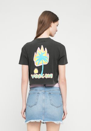 T-shirt noir court avec un motif coloré de palmier et de flammes dans le dos ; associé à une jupe en denim bleu clair à ourlet effiloché.
