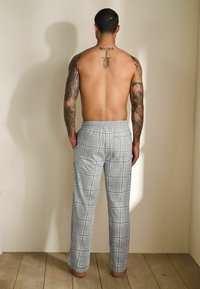 Šedé kárované tepláky s elastickým pásom, so bočnými vreckami a uvoľneným strihom. Hladký povrch na drevenej podlahe.