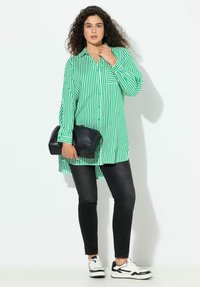 Camisa de manga larga a rayas verdes y blancas con cierre de botones y bolsillo, combinada con jeans ajustados negros y zapatillas blancas. Incluye bolso de mano negro.