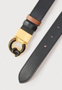 Juodas odinis diržas su auksinio atspalvio sagtimi, kurios dalis yra juoda. Rudos spalvos odinė detalė šalia sagties. Švelnios tekstūros ir apvalia galūne.