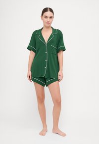 Conjunto de pijama de meia manga verde, feito de um tecido suave, com acabamentos brancos, um bolso na camisa e calções a condizer.