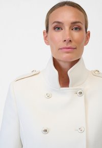 Witte double-breasted jas met een hoge kraag, zilveren knopen en textiel met een structuur, die een schone en gestructureerde uitstraling toont.