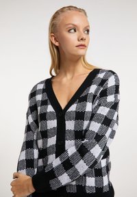 Cardigan în carouri alb-negru cu decolteu în V, având un tricot texturat, cinci butoane negre și mansete cu model elastic.