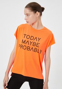 T-shirt z krótkim rękawem w jasnym pomarańczowym kolorze, wykonany z gładkiego, lekkiego materiału, z wyrazistym czarnym napisem: "DZIŚ MOŻE PRAWDPODOBNIE" na przodzie.