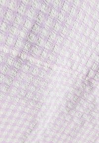 Lavendel- och vitmönstrad tyg med en texturerad, rutad design, som har en synlig söm. Mjuk, lätt textil.