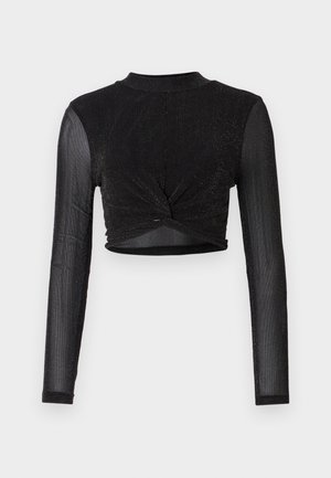 Melnā, garajām piedurknēm, īsā topā ar pagrieztu priekšpusi, izgatavots no mirdzoša, teksturēta auduma. Augsts kakla izgriezums un pieguloša forma.