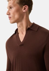 Brauner V-Ausschnitt-Pullover aus strukturiertem Strick, mit einem Kragen und einer taillierten Silhouette, an einem Modell, das im Profil dargestellt wird.