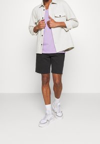 Ljusgrå, överdimensionerad skjorta med två bröstfickor, lager ovanpå en lavendelfärgad linne. Svarta denimshorts och vita sneakers med grå accenter.