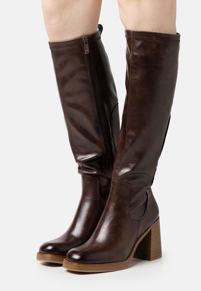 Ruskean nahkaiset polvipituiset saappaat, joissa on paksu puinen korko, sivuvetoketju ja sileä pinta. Leveä pohjeosa tarjoaa mukavan istuvuuden.