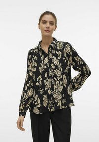 Sort bluse med et blomsterprint i beige, med knaplukning foran, krave og lange ærmer i en afslappet pasform.