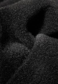 Svart tyg med en mjuk, texturerad yta som visar en tät stickning. Har en matt finish med lätt glans i vissa områden.