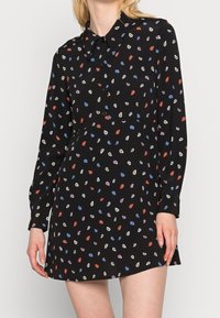 Czarna sukienka koszulowa z kołnierzykiem i długimi rękawami, ozdobiona małymi, kolorowymi wzorami liści. Miękka tkanina o luźnym kroju.