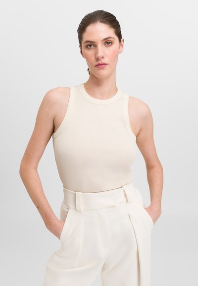 Débardeur beige à côtes avec un col haut et de larges bretelles, assorti à un pantalon crème taille haute avec poches latérales.