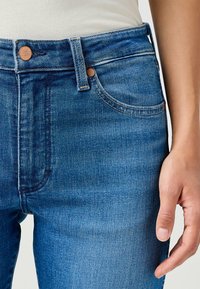 Blå denimjeans med hög midja, utrustade med kopparnitar, traditionell femfickdesign och en lätt blekt struktur på tyget.