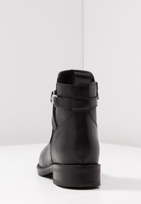 Black leather ankle boot with a smooth finish, rounded toe, side buckle detail, and low stacked heel. Rear view shows stitch accents.