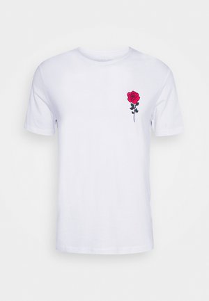 Camiseta de algodón blanca con una rosa bordada roja en el lado izquierdo del pecho, cuello redondo y mangas cortas. Textura suave, corte regular.