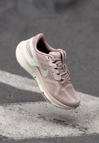 Light pink running shoe with a mesh upper, padded collar, and white Nike swoosh. Features a cushioned sole and textured outsole for grip.