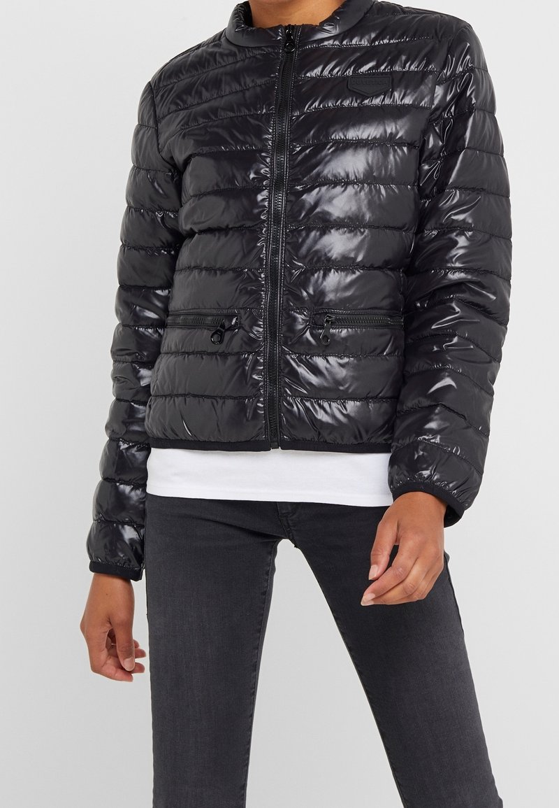 Black puffer jacket featuring a shiny, quilted texture, front zip closure, and two zippered pockets. Designed with a round neckline and elastic cuffs.