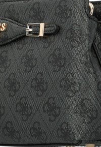 Schwarze Handtasche mit strukturiertem Material und geprägtem Logo-Muster, ausgestattet mit einer silberfarbenen Hardware-Schnalle und einem eleganten Design. Kompakte und strukturierte Form.