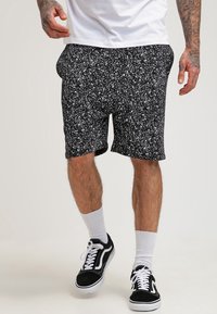 Czarne szorty z białym nakrapianym wzorem, wykonane z miękkiego materiału, z elastyczną talią i bocznymi kieszeniami, zestawione z czarnymi trampkami.