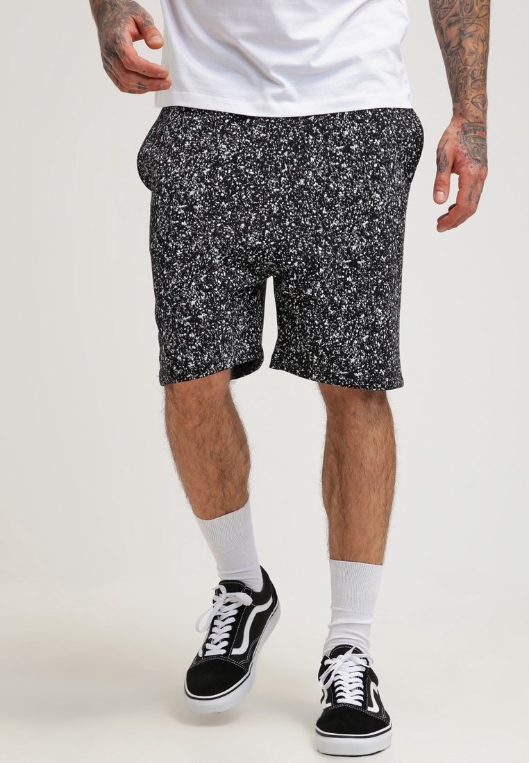 Czarne szorty z białym nakrapianym wzorem, wykonane z miękkiego materiału, z elastyczną talią i bocznymi kieszeniami, zestawione z czarnymi trampkami.