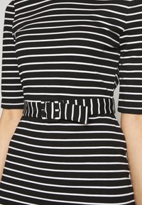 Czarna sukienka w białe paski z krótkimi rękawami, dopasowaną talią i paskiem w tym samym wzorze. Miękka tkanina o gładkiej fakturze.