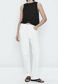 Débardeur noir noué, jeans blancs à jambes droites et sandales noires à lanières. Le tissu semble léger avec une finition texturée.