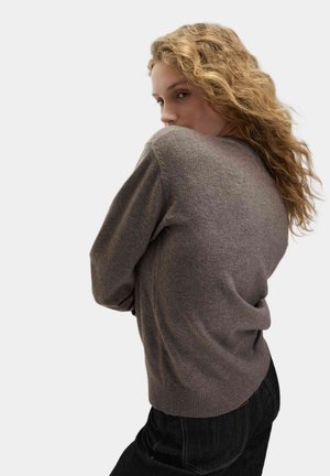 Brown knitted sweater with a relaxed fit, ribbed cuffs and hem, and a soft texture, paired with dark denim jeans.