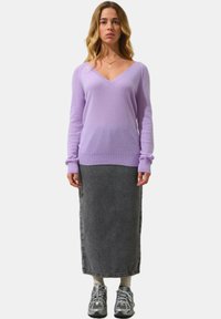 Maglione viola a scollo a V in materiale morbido, abbinato a una lunga gonna di denim grigia. Le calzature comprendono sneaker grigie con dettagli bianchi.