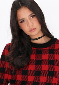 Rot-schwarz kariertes Strickpullover mit rundem Halsausschnitt und langen Ärmeln, das eine weiche Textur und ein schwarzes Choker-Accessoire bietet.
